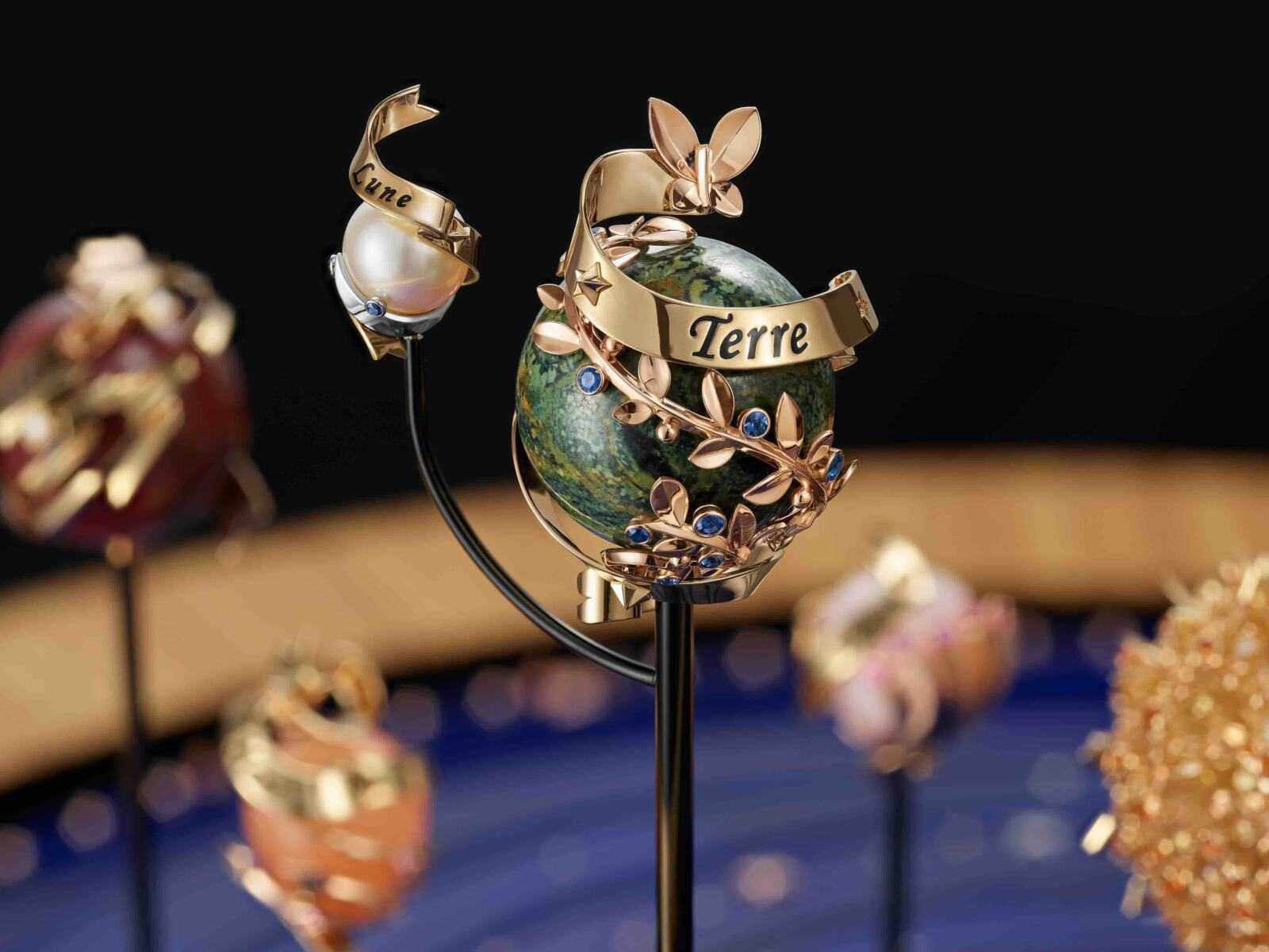 Extraordinary Objects Collection, Planétarium automaton. 50 cm x 66.5 cm base, rhodium plated 18K white gold, 18K rose gold, round diamonds, lapis lazuli, lemon tree, ziricote, amaranth, white holly, aluminum, steel, brass, black and bronze PVD, goat leather; 18K yellow gold and 18K rose gold Sun, round yellow sapphires, round spessartite garnets, round diamonds; rhodium plated 18K white gold and 18K yellow gold Mercury, round blue sapphires, calcedony; 18K rose gold and 18K yellow gold Venus, round pink sapphires, milky rose quartz; 18K rose gold and 18K yellow gold Earth, round blue sapphires, jasper; rhodium plated 18K white gold and 18K yellow gold Moon, round blue sapphires, pearl; 18K rose gold and 18K yellow gold Mars, round pink sapphires, orange moonstone; 18K yellow gold and 18K rose gold Jupiter, round diamonds, jasper; rhodium plated 18K white gold and 18K yellow gold Saturn, round blue sapphires, jet; 18K rose gold and rhodium plated 18K white gold shooting star, Traditional Mystery Set rubies, baguette-cut rubies, round diamonds; 18K yellow gold and 18K rose gold dials, lapis lazuli, black and bronze PVD, steel; 18K yellow gold hands; 18K yellow gold and 18K rose gold ON/OFF button, round diamond, bronze PVD; 18K rose gold lever, round diamond, ziricote, steel, bronze PVD; DEF, IF to VVS diamonds; manual-winding mechanical movement; planetarium module, perpetual calendar, hours/minutes dial, on-demand animation equipped with a carillon of 15 bells, 15-day power reserve; unique piece. © Van Cleef & Arpels